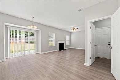 Unfurnished living room featuring a fireplace with raised hearth, light wood-style flooring, a chandelier, a textured ceiling, and a ceiling fan
