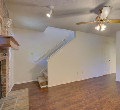 Unfurnished living room with dark wood-style floors, stairs, a brick fireplace, a textured ceiling, and a ceiling fan