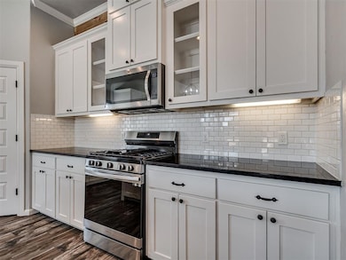 Kitchen featuring stainless steel appliances, decorative backsplash, white cabinets, dark stone countertops, and glass insert cabinets