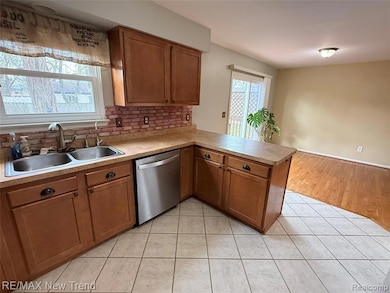 Kitchen with brown cabinets, light tile patterned floors, a peninsula, stainless steel dishwasher, and tasteful backsplash