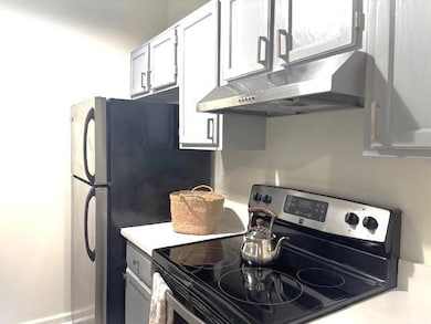 Kitchen with electric range, under cabinet range hood, light countertops, and white cabinetry