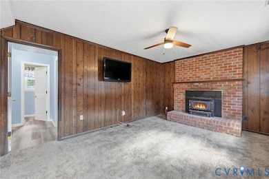 Unfurnished living room with wooden walls, carpet flooring, ceiling fan, a fireplace, and a textured ceiling