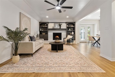 Living room with light wood-type flooring, a fireplace, crown molding, recessed lighting, and built in features