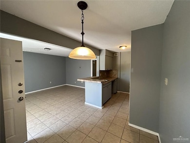 Kitchen with a peninsula, dark countertops, baseboards, decorative backsplash, and light tile patterned floors