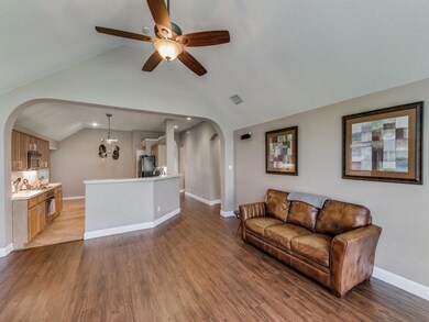 Living room with lofted ceiling, ceiling fan, wood-style flooring, opens to kitchen