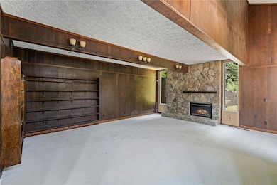 Unfurnished living room featuring finished concrete floors, wood walls, a fireplace, and a textured ceiling