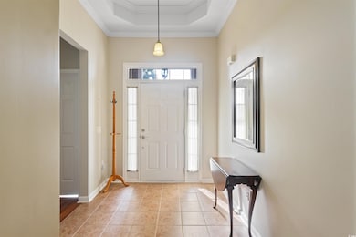 Foyer with ornamental molding, light tile patterned flooring, and a raised ceiling
