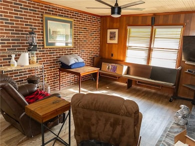 Living room with ceiling fan, hardwood / wood-style floors, wooden walls, and brick wall