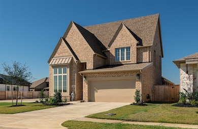 Modern two-story brick home with a pitched roof and large front window. It features a spacious driveway leading to a double garage and is surrounded by a well-maintained lawn and small trees.