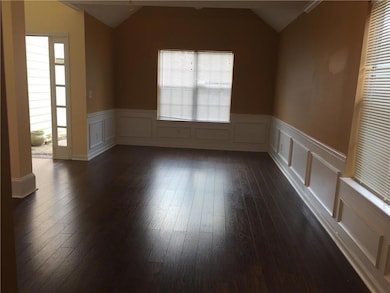 Spare room with lofted ceiling, dark wood finished floors, wainscoting, and a decorative wall