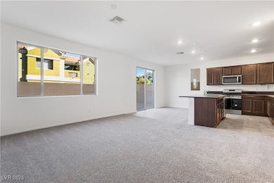 Kitchen with dark countertops, dark brown cabinets, open floor plan, a center island with sink, and light colored carpet
