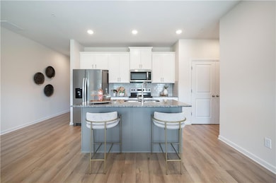 Kitchen with backsplash, light stone counters, stainless steel appliances, white cabinetry, and light wood finished floors