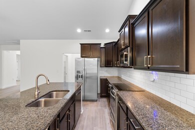 Kitchen with appliances with stainless steel finishes, dark stone countertops, light wood finished floors, dark brown cabinetry, and decorative backsplash