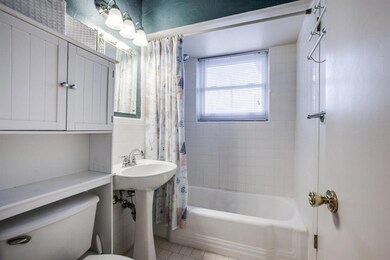 Full Bath adjacent to the Primary Bedroom has a pedestal sink, tub with shower, recently upgraded window (Renewal by Anderson), white tile flooring, & storage over the toilet.