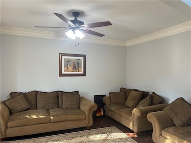 Living area with crown molding, dark wood-type flooring, and a ceiling fan