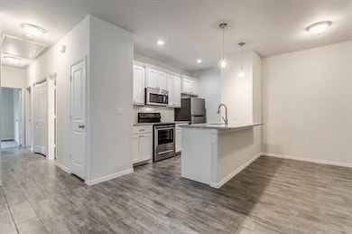 Kitchen featuring white cabinetry, stainless steel appliances, hanging light fixtures, dark wood-type flooring, and light countertops