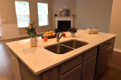 Kitchen featuring open floor plan, a kitchen island with sink, light stone counters, stainless steel dishwasher, and a fireplace