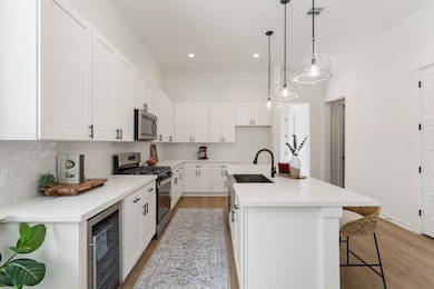 The open kitchen combines function and style with Whirlpool stainless steel appliances, a GE beverage center, and soft-closing white shaker cabinets.