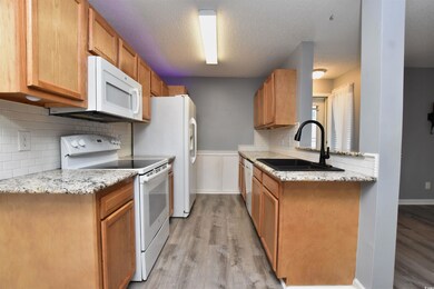 Kitchen featuring white appliances, light stone countertops, decorative backsplash, light wood-style floors, and a textured ceiling