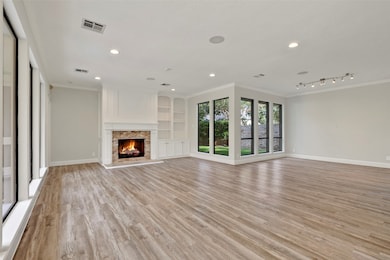 This spacious living room features large windows for natural light, a cozy fireplace with a stone surround, built-in shelving, and stylish wood flooring, creating a warm and inviting atmosphere.