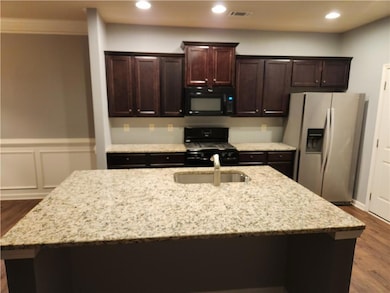 Kitchen featuring black appliances, an island with sink, a sink, dark wood-style floors, and dark brown cabinetry