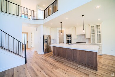 Kitchen with recessed lighting, a towering ceiling, an island with sink, stainless steel appliances, and dark brown cabinets