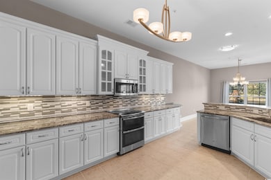 Kitchen featuring a chandelier, hanging light fixtures, glass insert cabinets, stainless steel appliances, and dark stone counters
