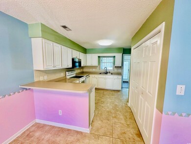 Kitchen with white electric stove, white cabinetry, a peninsula, decorative backsplash, and light countertops