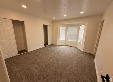 Unfurnished bedroom featuring dark colored carpet, recessed lighting, two closets, and a textured ceiling