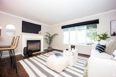 Living area with ornamental molding, wood finished floors, a fireplace with flush hearth, and baseboard heating. Home is now vacant - these photos are provided to envision the room decorated.