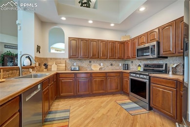 Kitchen featuring appliances with stainless steel finishes, brown cabinets, light countertops, light wood-type flooring, and decorative backsplash