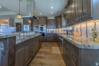 Kitchen featuring island range hood, decorative backsplash, stainless steel appliances, dark brown cabinetry, and recessed lighting