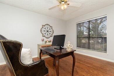 The study features elegant wood floors, a ceiling fan and a large window looking out to the front yard.