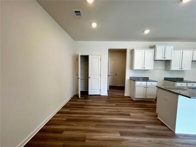 Kitchen featuring white cabinets, dark wood-style floors, recessed lighting, dark stone countertops, and vaulted ceiling