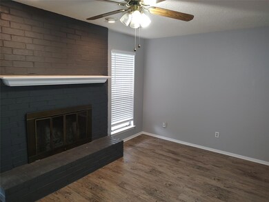 Unfurnished living room featuring wood finished floors, a ceiling fan, and a brick fireplace