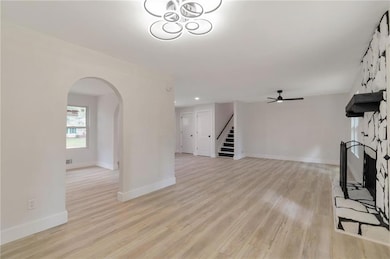 Unfurnished living room with stairs, arched walkways, light wood-style flooring, a ceiling fan, and a large fireplace