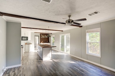 Kitchen with butcher block countertops, a textured ceiling, white cabinetry, beam ceiling, and dark wood-type flooring
