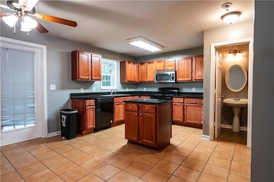Kitchen with black appliances, dark countertops, light tile patterned floors, a ceiling fan, and a sink