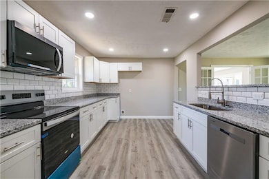Kitchen featuring light stone counters, a sink, stainless steel appliances, visible vents, and white cabinets