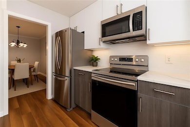 Kitchen featuring appliances with stainless steel finishes, modern cabinets, white cabinetry, ornamental molding, and dark wood-type flooring