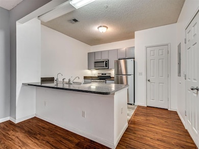 Kitchen with stainless steel appliances, a peninsula, gray cabinetry, dark wood finished floors, and a textured ceiling