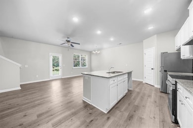 Kitchen with stainless steel range with electric cooktop, a sink, ceiling fan, an island with sink, and white cabinetry