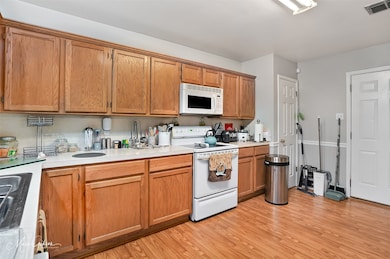 Kitchen featuring white appliances, light wood-type flooring, light countertops, and brown cabinetry