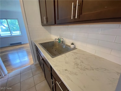 Kitchen featuring dark brown cabinetry, light tile patterned flooring, decorative backsplash, and light stone countertops