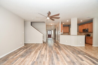 This is a spacious, open-concept living area with wood-look flooring and a kitchen featuring wooden cabinetry and modern appliances. The room is well-lit and includes a ceiling fan, with a staircase leading to the upper level.