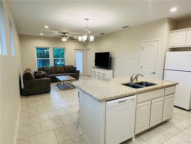 Kitchen with hanging light fixtures, white appliances, an island with sink, white cabinetry, and sink