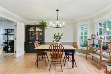 Dining room featuring light wood-style flooring, a chandelier, ornamental molding, and baseboards