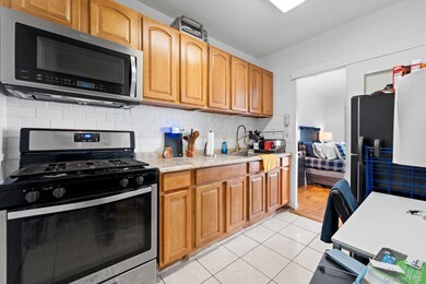 Kitchen with stainless steel appliances, backsplash, light tile patterned floors, and light stone countertops