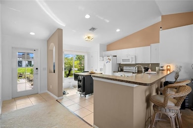 Kitchen with light tile patterned floors, a peninsula, a breakfast bar area, white cabinetry, and vaulted ceiling