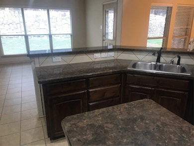 Kitchen featuring a sink, light tile patterned floors, dark brown cabinetry, and dark stone countertops